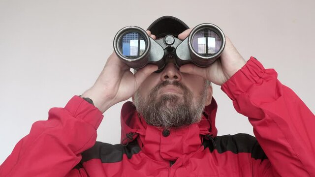 Man in red coad looks ahead through binoculars. Watching faraway objects.