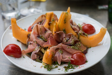 closeup of salad  with ham, melon and vegetables in a white plate on the table at the restaurant
