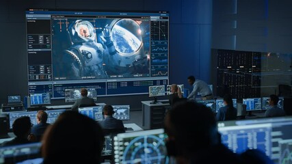 Group of People in Mission Control Center Establish Successful Video Connection on a Big Screen with an Astronaut on Board of a Space Station. Flight Control Scientists Sit in Front of Computers.