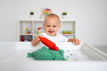Baby playing with green kinetic sand and rolling pin. Little girl playing with sand at home, games, education, children room