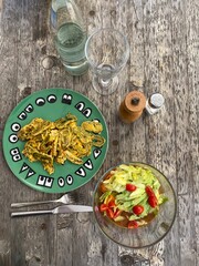 Gebratene Gemüsemaultaschen auf grünen Teller daneben frischer bunter Salat Besteck Glas Flasche Wasser Pfeffermühle Salzstreuer