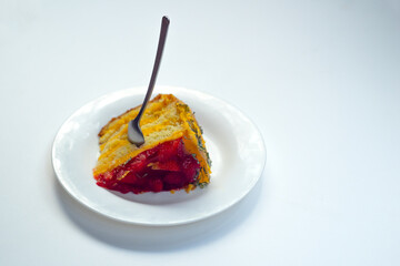 White glass plate with a piece of cake with strawberries, a spoon stuck on top.On a white isolate, place for the inscription.