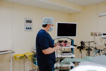 Adult male doctor at blue medical smock configuring medical equipments at the operation room. Copy space.