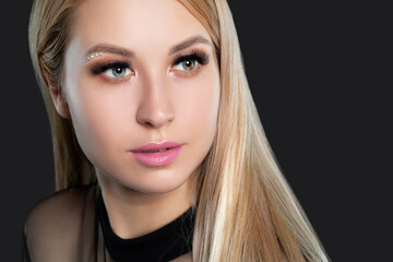 Naklejka premium Woman's blue green eye with pupil heterochromia, with long blond hair with beautiful make-up and thick eyebrows. Looking at the camera. Professional makeup and cosmetology.