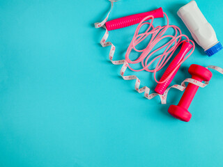 Dumbbell, skipping rope and ener

A pink dumbbell, a skipping rope and an energy drink in a bottle lay on the left against a blue background and in the space for text on the left, a close-up top view.