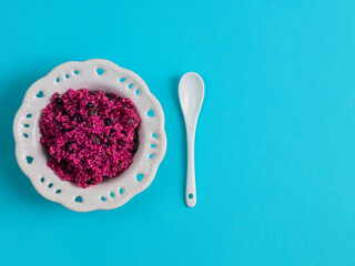 Pink quinoa with beets and beans.

Pink Quinua with beets and beans in a white plate with a spoon on a blue background on the left and space for text on the right, top view close-up.