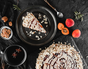 Almond cake with fresh apricot, nuts, and baking ustensils on dark background. Holiday cake, delecious sweets and dessert, top up view