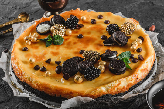 Classic Cheesecake With Caramel, Mini Oreos, Mint Leaves, And Berries On Paper Over Dark Background, Close Up View. Delecious Sweets And Dessert