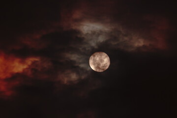 bright full moon, covered by a veil of dark clouds shaded by red.