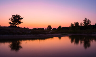 Fototapeta na wymiar quiet smal lake at the twilight, forest silhouette on a pink sky