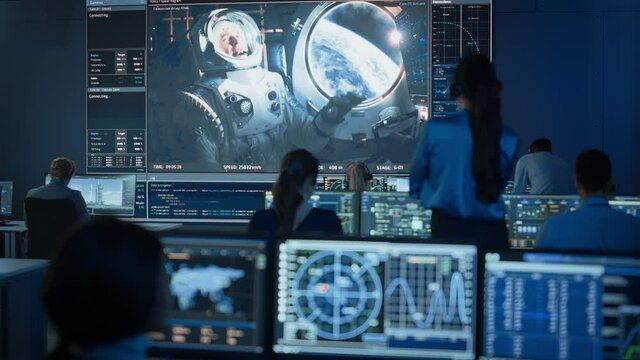 Group of People in Mission Control Center Establish Successful Video Connection on a Big Screen with an Astronaut on Board of a Space Station. Flight Control Scientists Sit in Front of Computers.