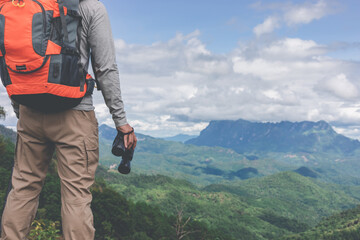 Young man with backpack and holding a binoculars looking on top of mountain