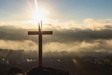 Silhouettes of crucifix symbol with bright sunbeam on top of mountain.