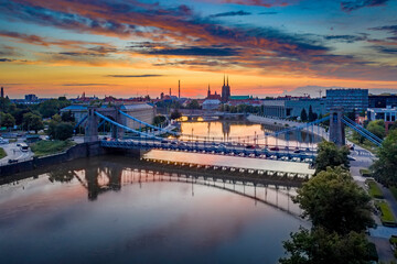 Drone view on the Grunwaldzki Bridge above Oder river in Wrocław at beautiful sunset. Rushing traffic, illuminated historic buildings and bridges. Beautiful sky, light reflections on the blurry water - obrazy, fototapety, plakaty