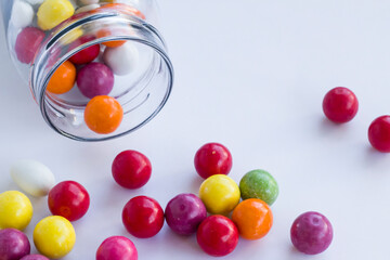 Colorful candies in transparent glass bowl on grey background with overturned jar.