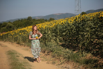 Fototapeta premium Beautiful young woman in a field of sunflowers in a green dress