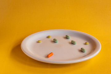 White plate with colored medications on a orange background. Pharmaceutical drug overdose concept.
