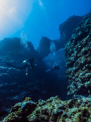 Scuba diver and coral reef with sunlight. Divers are going into the underwater valley. Island, Okinawa, Japan 