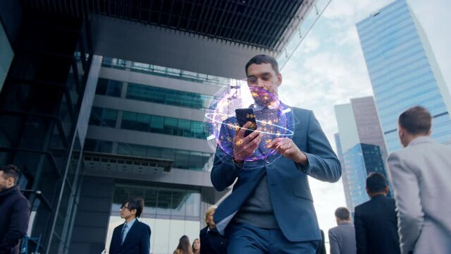 Handsome Businessman Uses Smartphone with Animated Infographics Showing Internet Icons, Walks through Crowded City Streets. Big Data, Information, e-Business Concept. Moving Low Angle Front View