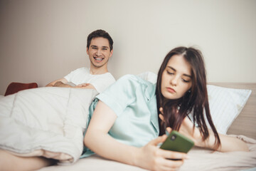 Smiling caucasian man waiting for his wife to write a message on phone in bed
