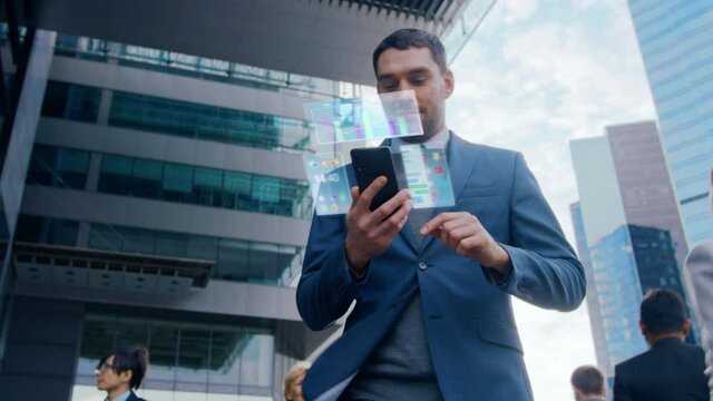 On Busy City Street Handsome Businessman Uses Smartphone with Animated Holographic Screens Show Business Graphs, Charts and Stock Market Analysis Statistics. Mock-up Mobile OS UI/UX. Moving Front View