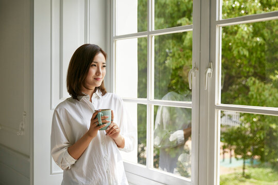 young asian woman looking out of window at home