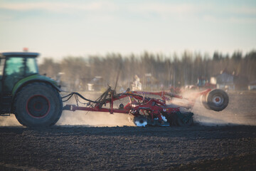Tractor with a disc harrow system harrows the cultivated farm field, process of harrowing and preparing the soil, tractor seeding crops at field on sunset, agriculture concept, harrow machine at work