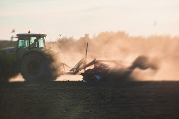 Tractor with a disc harrow system harrows the cultivated farm field, process of harrowing and preparing the soil, tractor seeding crops at field on sunset, agriculture concept, harrow machine at work