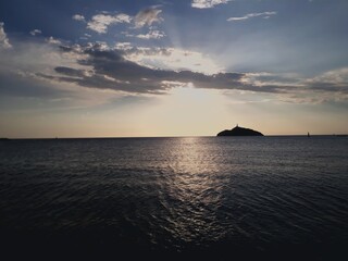 View of the Ocean Background sun into clouds and an island. Island Silhouette in the Ocean. Sunligth between clouds

