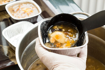 Gloved hand is serving dessert ashura with black ladle,close up
