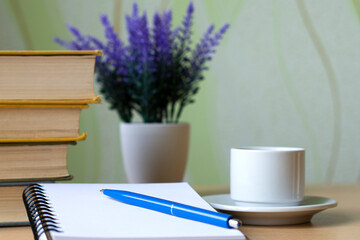 A notebook with white pages lies on the table against a background of lavender, cups and textbooks.