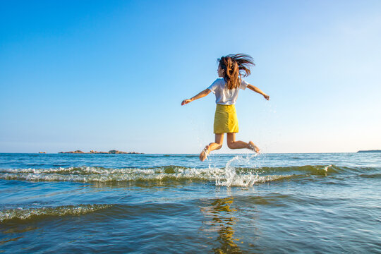 Under the blue sky, a girl with long hair jumping on the beach