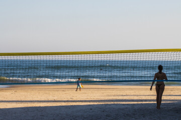 Rede de vôlei armada na praia com sombra de mulher em segundo plano