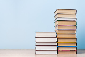Two stacks of books of different heights stand on a wooden table against a light blue wall, space for text