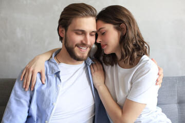 Young loving couple relaxing on sofa together. Woman and man embrace enjoy company of each other sitting on couch holding hands having romantic date.