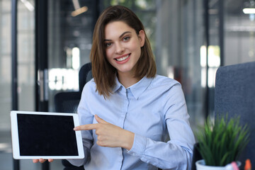 Young happy business woman showing blank tablet computer screen in office.