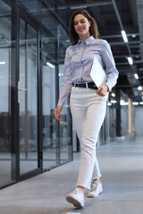 Businesswoman walking along the office corridor with documents.