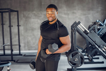 Obraz na płótnie Canvas Sports man in the gym. A black man performs exercises. Guy in a black t-shirt