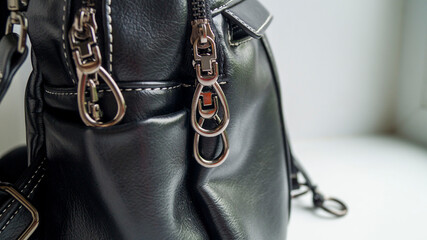 Locks on a woman's bag. Black bag on a light background. An accessory for a fashionable look. Women's bag-backpack. Convertible bag. Selective focus.