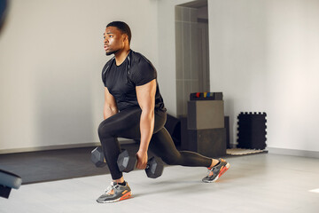 Sports man in the gym. A black man performs exercises. Guy in a black t-shirt
