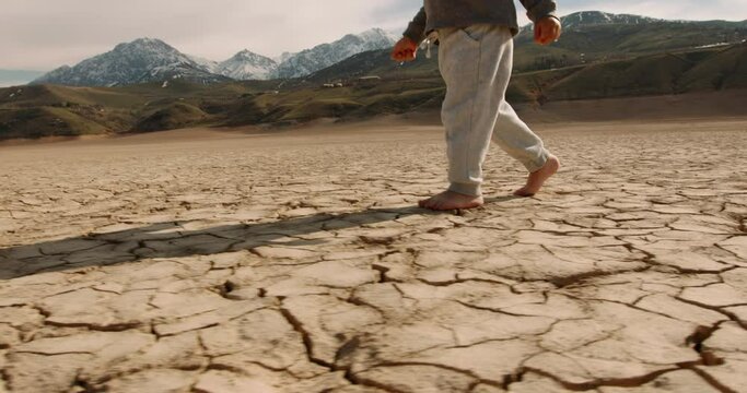 Close up shot of legs of baby boy running on cracked ground, destroyed by erosion, desertification and global warming - environmental issues, save our planet 4k footage