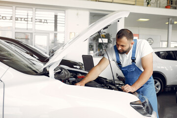 Wrker in a car salon. Expert checks the car. Man in a blue uniform.