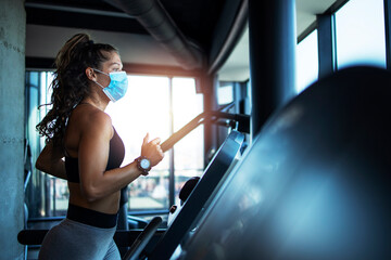 Fototapeta na wymiar Sportswoman training on treadmill in gym and wearing face mask to protect herself against coronavirus during global pandemic of covid-19 virus.