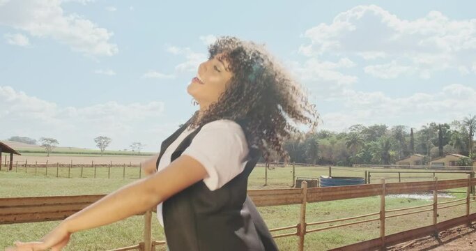 Young curly haired farmer woman dancing and walking along a dirt road on the farm. Cinematic 4K.