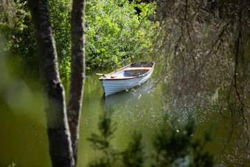 white rowboat seen between trees in lake with greenery
