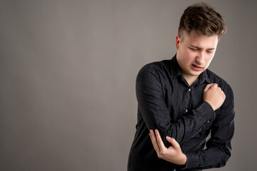 Portrait of serious stylish attractive man dressed with a casual black shirt gesturing elbow ache