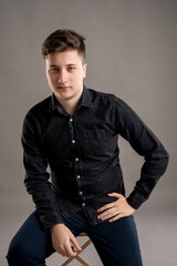 Fototapeta premium Portrait of serious stylish attractive man stading on the chair dressed with a casual black shirt