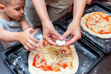 little boy helping mom make pizza at home