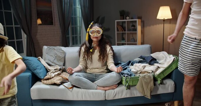 Funny asian family of three happy about upcoming vacation. Mother wearing scuba diver mask meditating while husband and kid are dancing near suitcases - travelling, happy family 4k footage