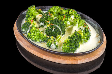 Tasty broccoli with cheese in a plate on wooden board with reflection, isolated on black background
